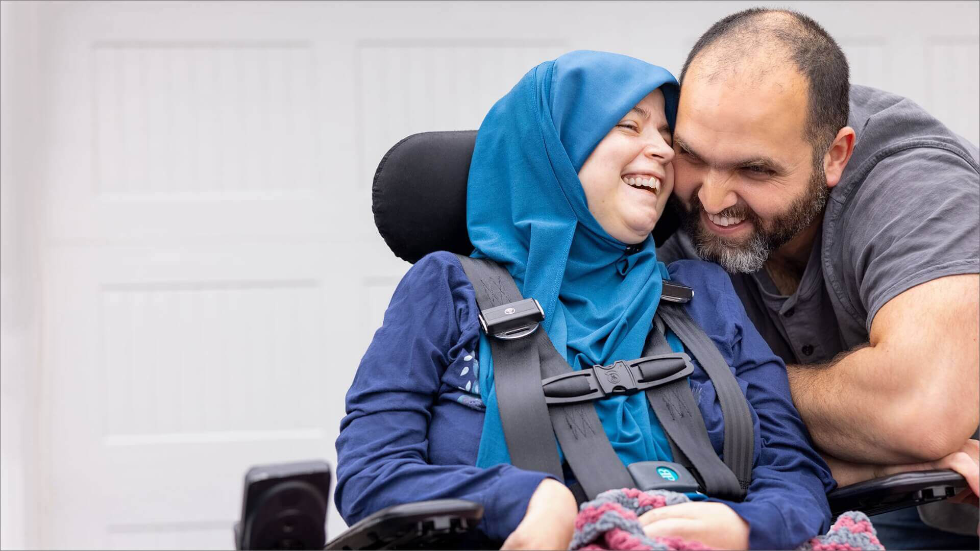 Smiling ALS patient in motorized chair next to smiling caregiver