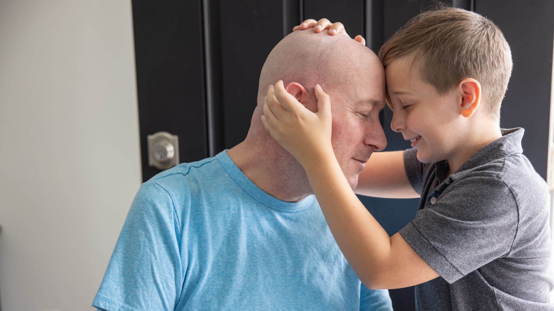 ALS patient and smiling child hugging with closed eyes