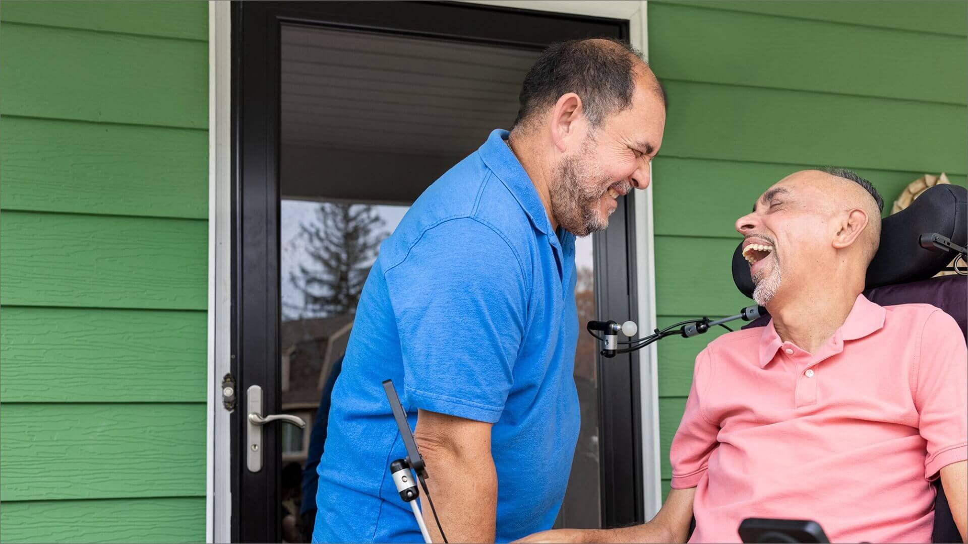 Laughing ALS patient in motorized chair next to smiling caregiver