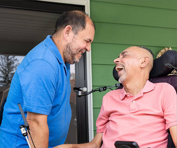 Laughing ALS patient in motorized chair next to smiling caregiver