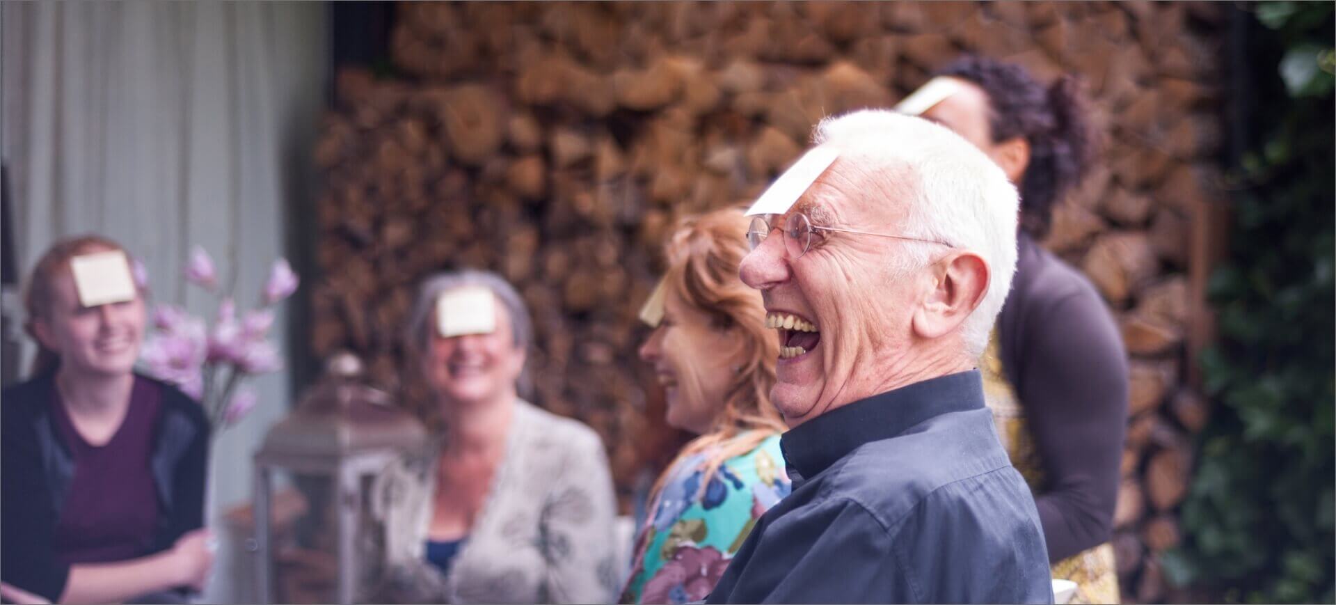 Man smiling in the foreground with a notecard on his forehead with other participants in the activity in the background