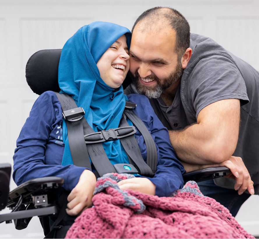 Person living with ALS in a motorized chair and their caregiver smiling