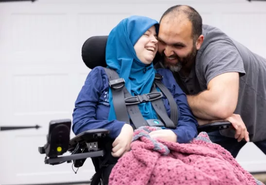 Smiling ALS patient in motorized chair next to smiling caregiver