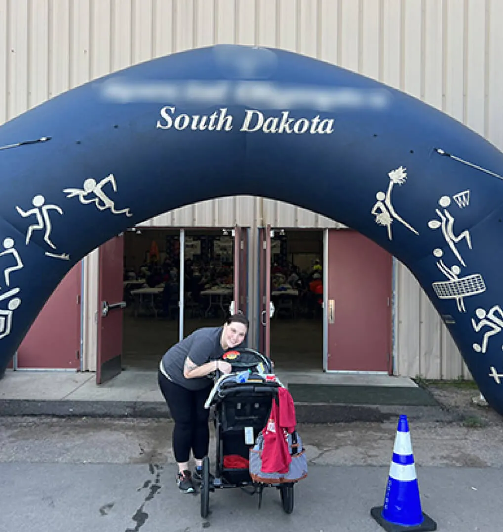 Woman posing with a stroller under a Special Olympics arch